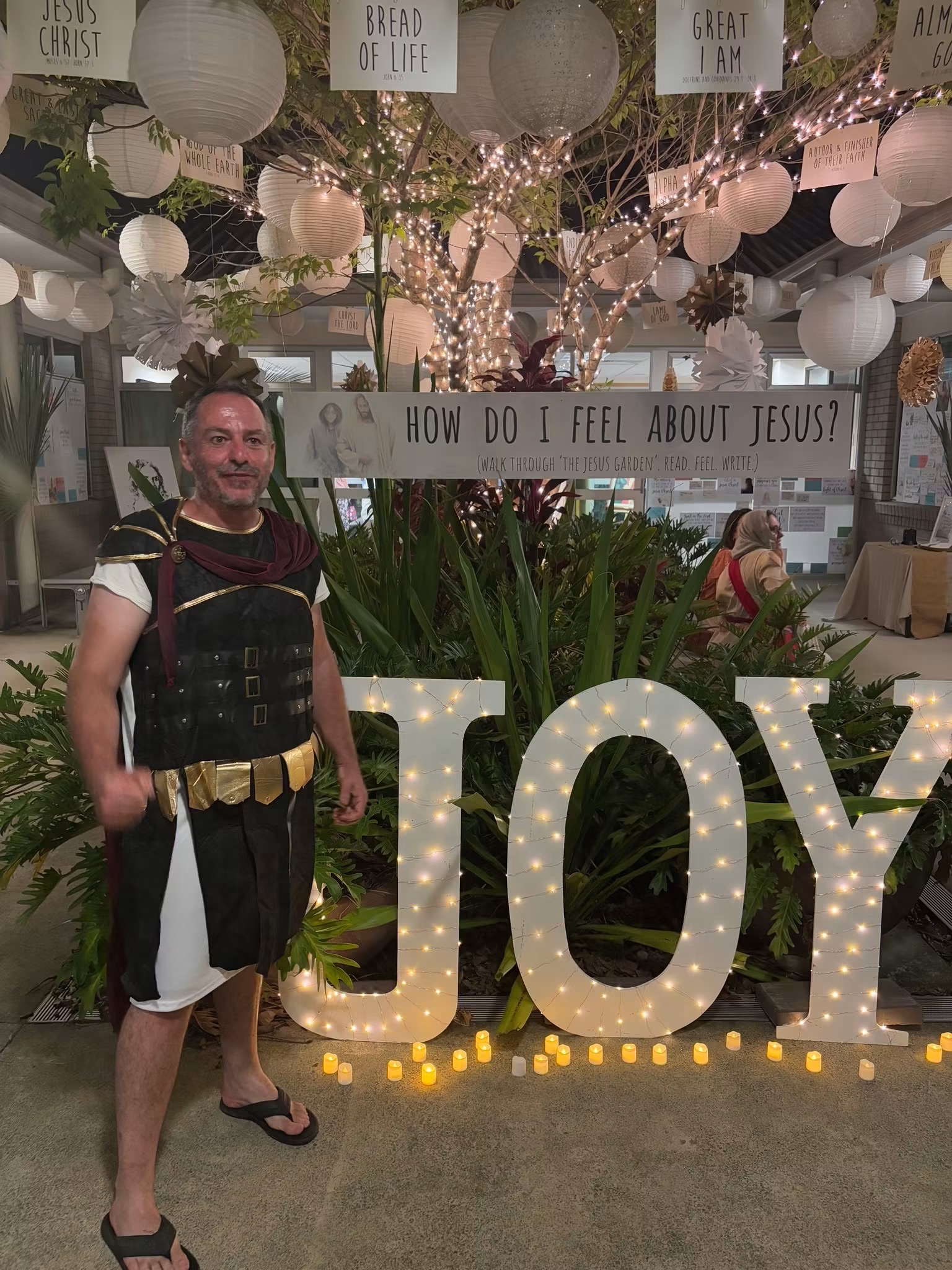 A Roman soldier in costume standing beside the illuminated JOY sign