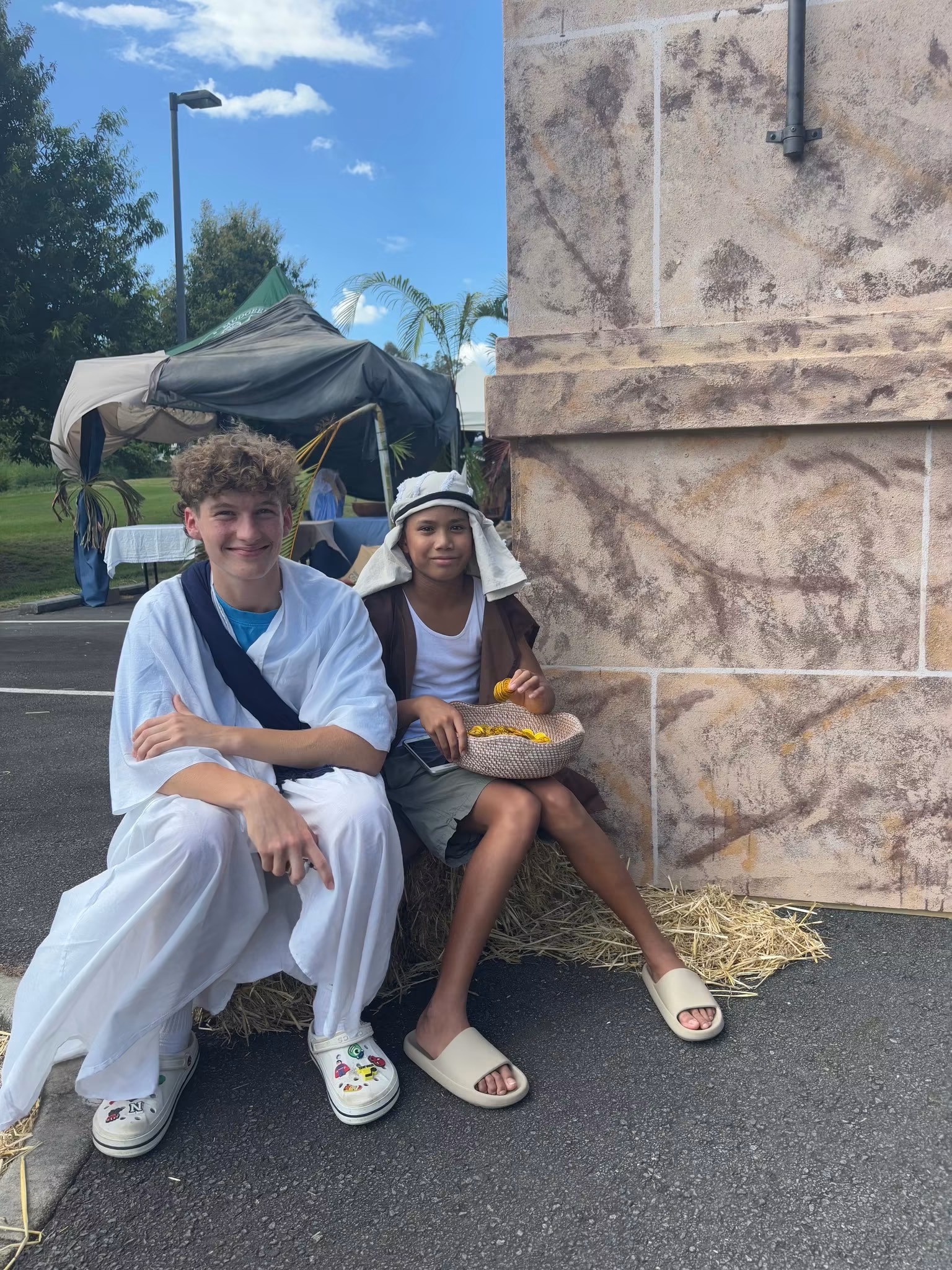 Two young people in costume sitting together against a stone wall