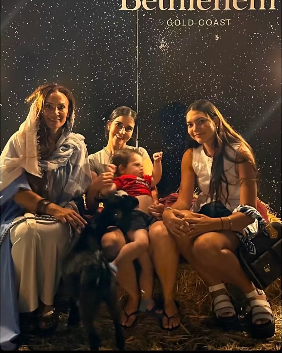 Three women in costume holding a baby in front of a star-lit backdrop