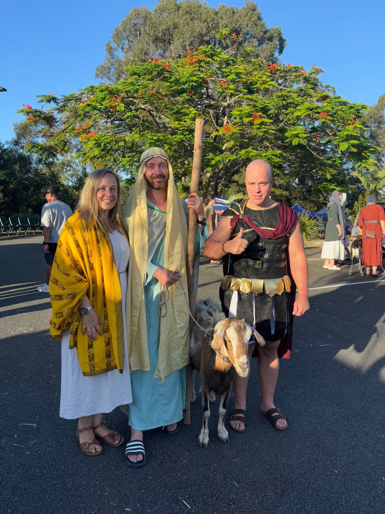 Two villagers and a Roman soldier in costume standing with a goat on a sunlit street